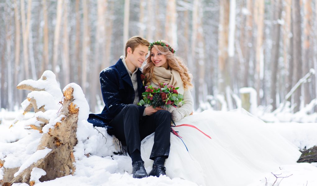 Mariée en robe blanche et étole chaude avec son marié dans une forêt enneigée