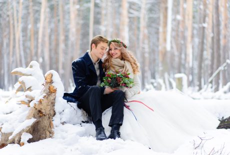 Mariée en robe blanche et étole chaude avec son marié dans une forêt enneigée
