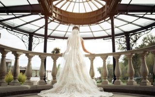 Mariée de dos en robe de dentelle ajustée à traîne et long voile, sous une rotonde