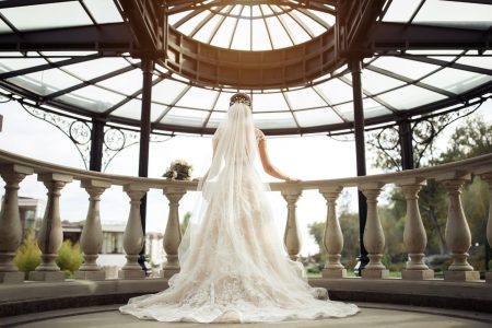 Mariée de dos en robe de dentelle ajustée à traîne et long voile, sous une rotonde