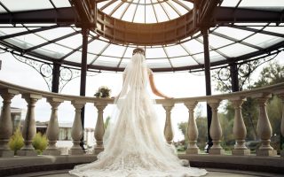 Mariée en robe blanche en dentelle avec un long voile, de dos sur un balcon baroque