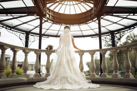 Mariée en robe blanche en dentelle avec un long voile, de dos sur un balcon baroque