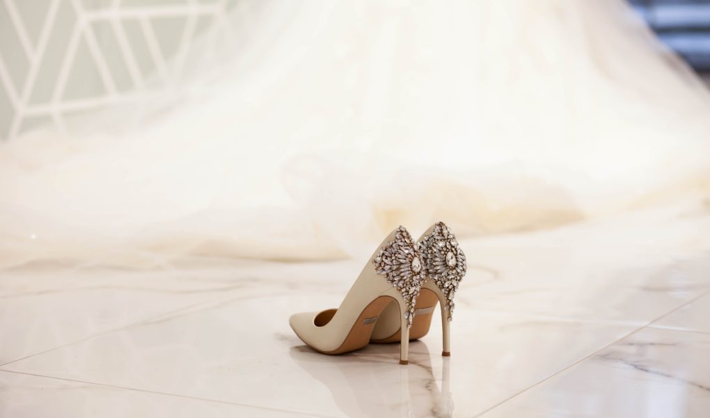 Escarpins de mariée ivoire ornés de bijoux, posés devant une longue robe de mariée
