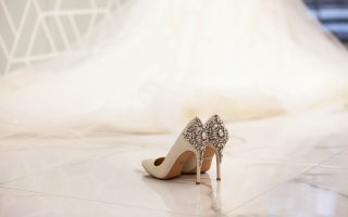 Escarpins de mariée ivoire ornés de bijoux, posés devant une longue robe de mariée