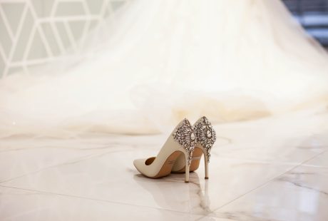 Escarpins de mariée ivoire ornés de bijoux, posés devant une longue robe de mariée