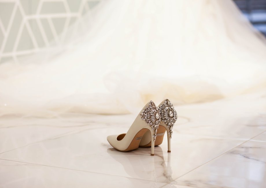 Escarpins de mariée ivoire ornés de bijoux, posés devant une longue robe de mariée