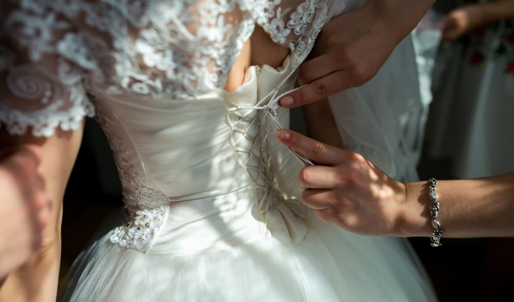 Préparatifs de la mariée : laçage du corset de la robe de mariée avant la cérémonie