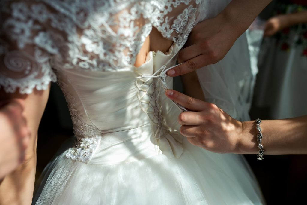 Préparatifs de la mariée : laçage du corset de la robe de mariée avant la cérémonie