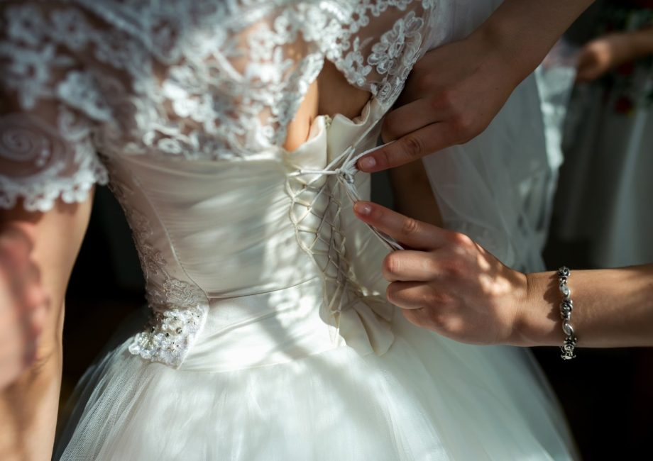 Préparatifs de la mariée : laçage du corset de la robe de mariée avant la cérémonie