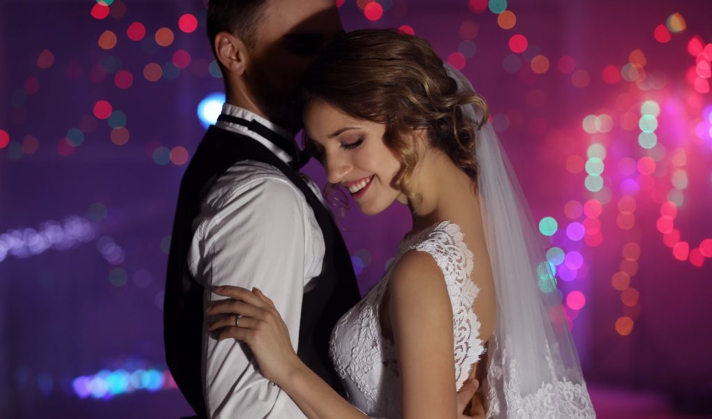 Mariée en robe de dentelle et voile enlaçant son époux pendant la soirée dansante