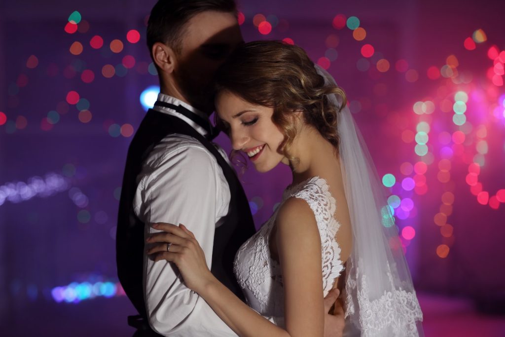 Mariée en robe de dentelle et voile enlaçant son époux pendant la soirée dansante