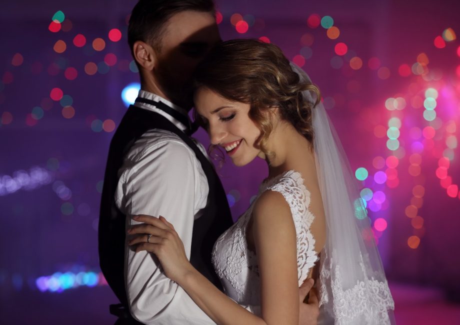 Mariée en robe de dentelle et voile enlaçant son époux pendant la soirée dansante